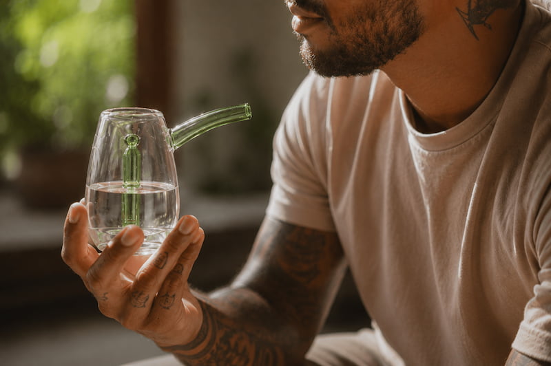 Man with tattoos holding a glass pipe bubbler